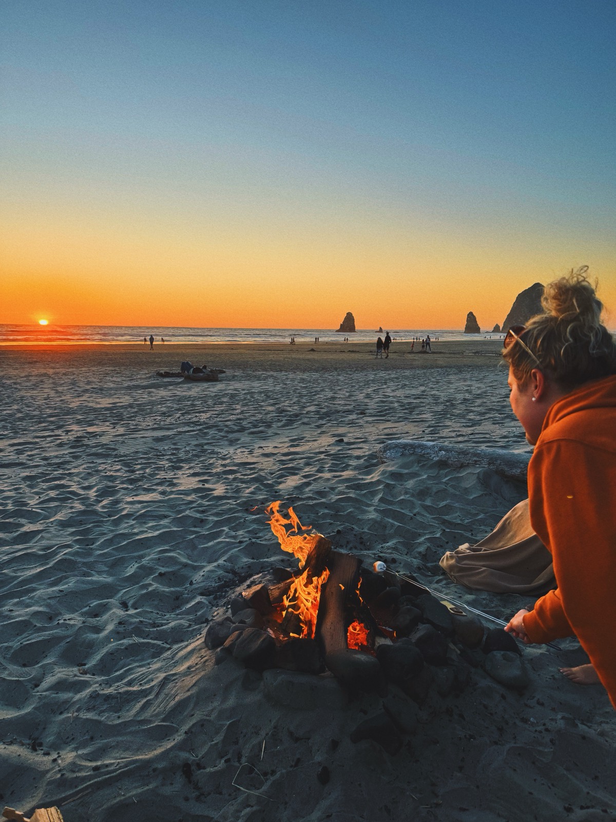 A beach campfire at sunset with sea stacks on the horizon