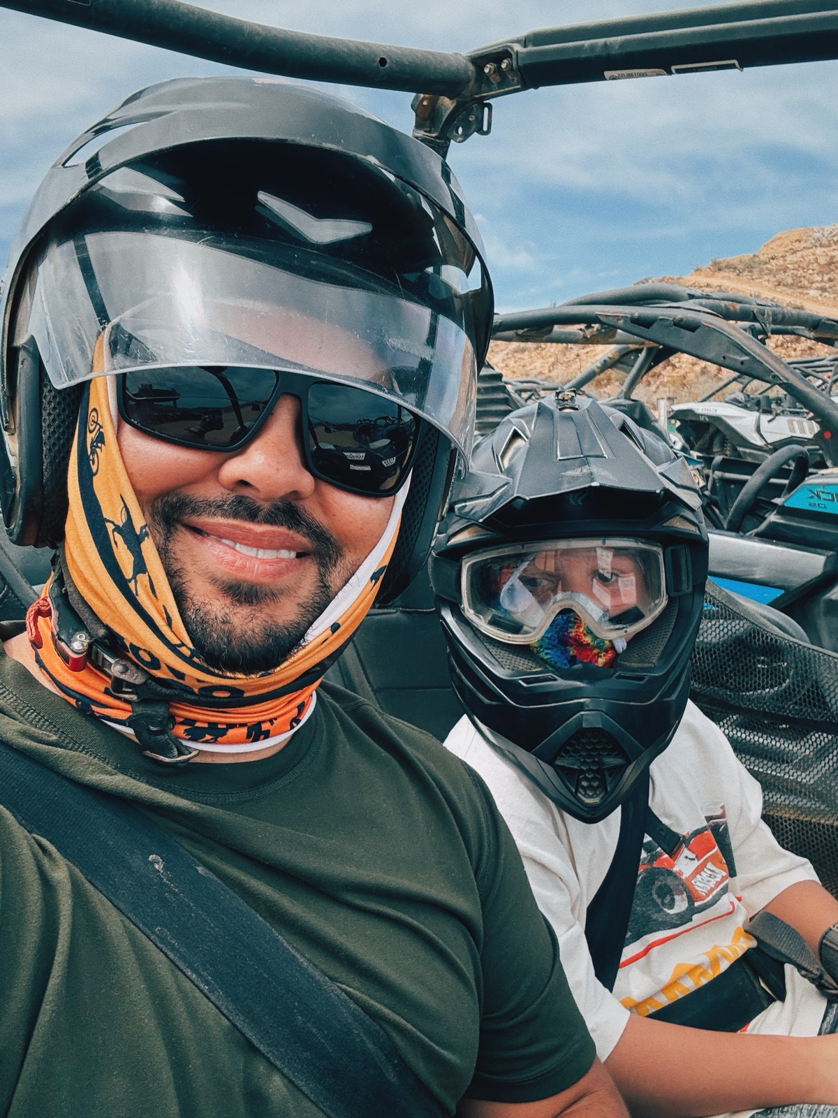 Selfie from an off-road buggy, helmets on, desert hills behind